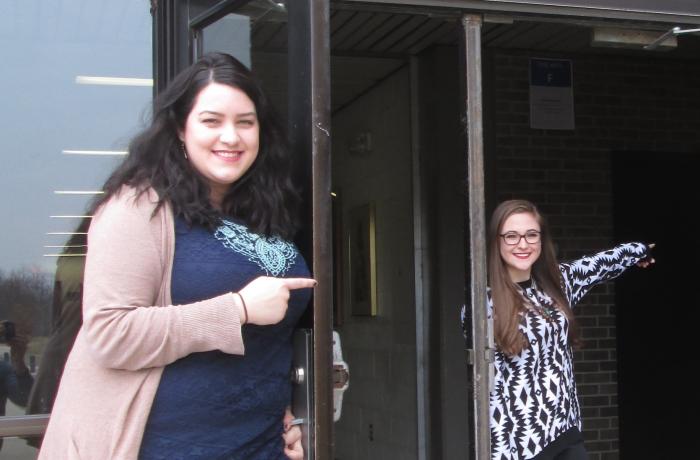 2016 Henry Ford College Annual Student Exhibition Two students pointing the way towards the gallery inside.