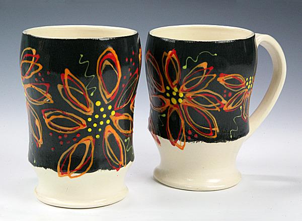 A pair of hand thrown ceramic mugs with multicolored decoration on white clay.