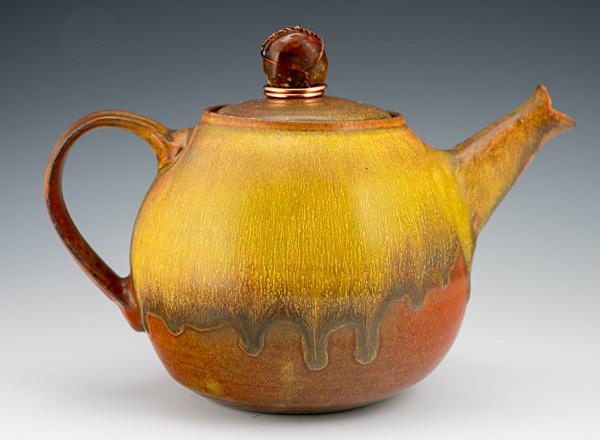 A hand thrown ceramic teapot with a rustic orange glaze.
