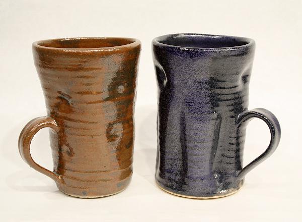 Pair of hand thrown drinking mugs: one with brown glaze and one with blue glaze.