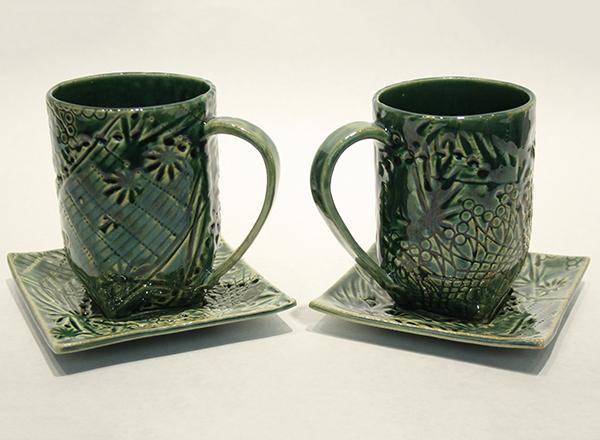 A pair of hand made, green glazed, ceramic cups and saucers.